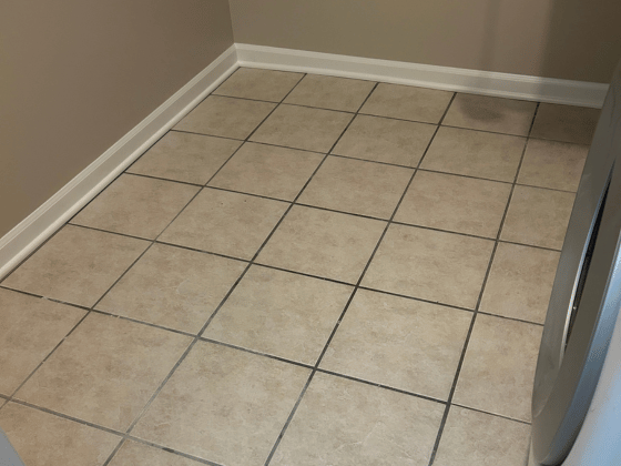 Tile floor in a laundry area with beige ceramic tiles and a washing machine to the right.