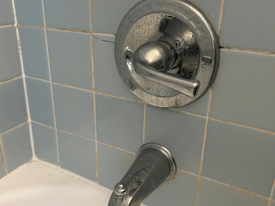 Close-up of a chrome bathtub faucet and round control knob on blue tiled bathroom wall.